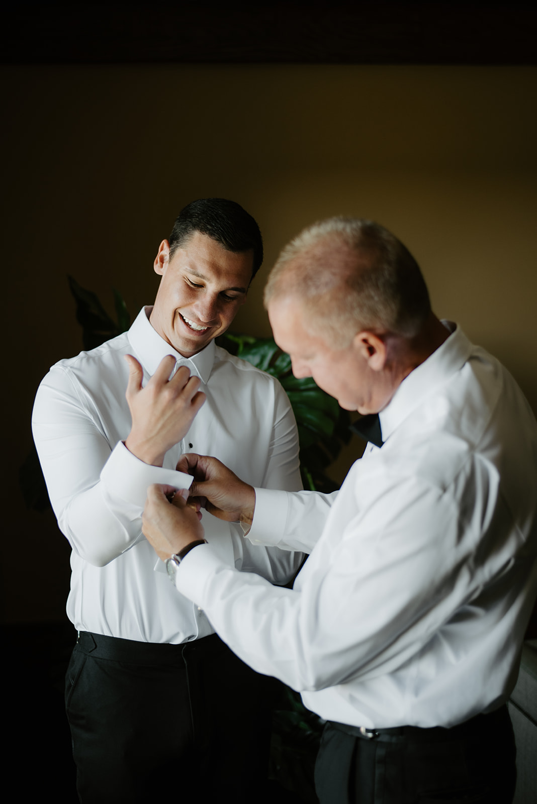 Father helping the groom adjust his white shirt cuffs during prep before the wedding ceremony.